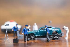 polizia in miniatura e detective in piedi intorno a una macchina, concetto di indagine sulla scena del crimine foto