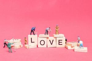 lavoratore in miniatura collaborando per costruire la parola amore su blocchi di legno con uno sfondo rosa, concetto di San Valentino foto