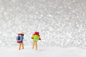 Backpackers in miniatura camminando su uno sfondo di neve, concetto di inverno foto