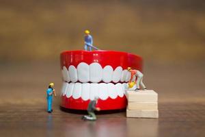 lavoratori in miniatura che riparano un dente, assistenza sanitaria e concetto medico foto