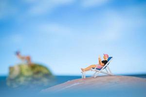 persone in miniatura che prendono il sole su una conchiglia con uno sfondo di cielo blu, concetto di vacanza estiva foto