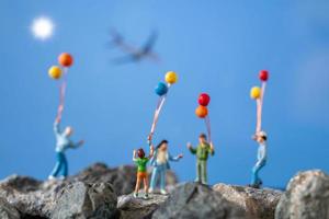 famiglia in miniatura tenendo palloncini su una roccia con uno sfondo di cielo blu foto