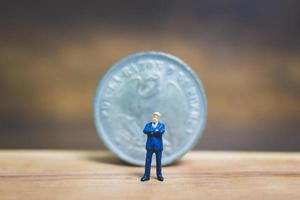 uomo d'affari in miniatura in piedi vicino a una moneta con uno sfondo di legno, concetto di business foto