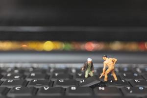 squadra in miniatura di ingegneri che riparano un computer portatile con tastiera, concetto di riparazione del computer foto