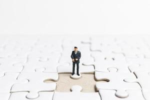 imprenditore in miniatura in piedi su un puzzle bianco, concetto di business foto
