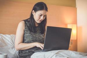 donna seduta sul letto, lavorando sul computer portatile foto