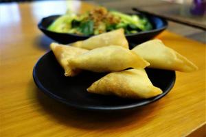 Samosa su un' nero piatto come un' vicino su con verde verdure nel il sfondo foto