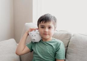 ragazzo felice che tiene salvadanaio con la faccia sorridente. ritratto dell'interno di un bambino allegro che mostra la scatola di risparmio dei soldi il bambino della scuola impara la responsabilità finanziaria e pianifica il risparmio per il concetto futuro foto