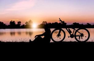 silhouette donna sedersi vicino bicicletta su tramonto. foto