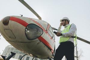 asiatico uomo aero ingegnere Lavorando su elicottero nel hangar guardare a digitale tavoletta foto