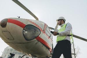 asiatico uomo aero ingegnere Lavorando su elicottero nel hangar guardare a digitale tavoletta foto