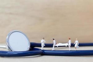 medici in miniatura con infermieri che trasportano un paziente su una barella, concetto di assistenza sanitaria foto