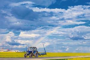 trattore su il campo. trattore cavalcate vicino il campo con un' arcobaleno foto