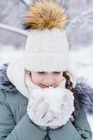 un' ragazza nel caldo Abiti detiene neve nel sua mani nel guanti nel un' inverno parco. inverno stile di vita ritratto. verticale Visualizza foto