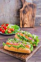 fresco caldo cani con salsiccia, cetriolo, pomodoro e erbe aromatiche su un' di legno tavolo. veloce cibo a casa. verticale Visualizza foto