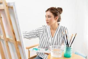 bellissimo femmina Hobby di artista e uso pennello nel astratto arte per creare capolavoro. pittore dipingere con acquerelli o olio nel studio Casa. godere pittura come passatempo, ricreazione, ispirazione foto