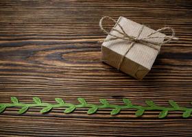 regalo. un' scatola di kraft carta legato con iuta corda su un' vecchio, di legno sfondo decorato con verde nastro con le foglie foto