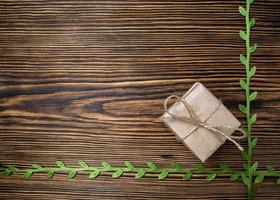 regalo. un' scatola di kraft carta legato con iuta corda su un' vecchio, di legno sfondo decorato con verde nastro con le foglie foto