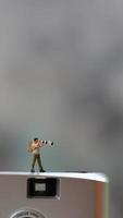un' miniatura figura assunzione immagine con un' telecamera contro un' vero telecamera nel il sfondo. foto