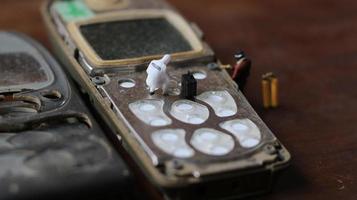 miniatura figura di un' tecnico riparazione un vecchio rotto cellula Telefono. Lavorando tecnico concetto. foto