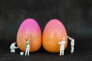 persone in miniatura che dipingono le uova di Pasqua per il giorno di Pasqua su uno sfondo nero foto