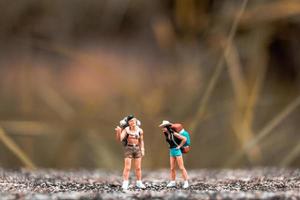 backpackers in miniatura in piedi su un pavimento di cemento con uno sfondo di natura bokeh foto