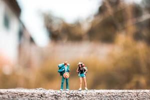 backpackers in miniatura in piedi su un pavimento di cemento con uno sfondo di natura bokeh foto