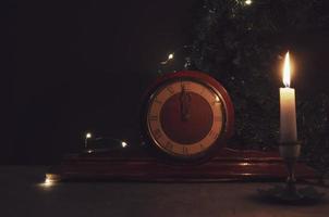 Vintage ▾ vecchio di legno orologio, giallo candela e Natale albero ramo su sfondo. mezzanotte su orologio. ardente candela. foto