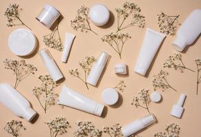 bianca plastica tubi, barattoli, e gypsophila rami su un' beige sfondo, contenitori per cosmetico creme e gel, pubblicità e marca promozione, superiore Visualizza foto