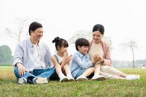 Immagine di un asiatico famiglia seduta insieme su il erba a il parco foto