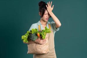 asiatico ragazza ritratto Tenere un' Borsa di verdure su un' verde sfondo foto