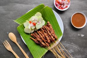 pollo satay o pollo satay servito con lungo, riso torta e arachide salsa. servito su Banana partire foto