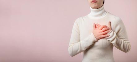 giovane donna sofferenza a partire dal cuore attacco su leggero rosa studio sfondo. doloroso crampi, cuore patologia, urgente su il petto con doloroso espressione. assistenza sanitaria mondo Salute giorno concetto. foto