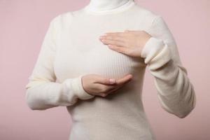 donna mani controllo granuli su sua Seno per segni di Seno cancro su rosa sfondo. assistenza sanitaria mondo Salute giorno concetto. foto