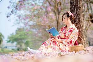 signora nel tradizionale chimono vestito lettura libro a ciliegia fiorire albero nel primavera Festival. foto