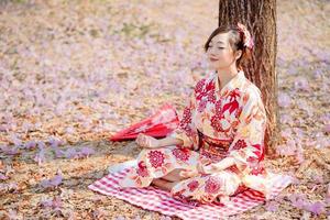 asiatico donna nel tradizionale chimono vestito pratiche meditazione a ciliegia fiorire albero. foto