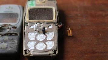 miniatura figura di un' tecnico riparazione un vecchio rotto cellula Telefono. Lavorando tecnico concetto. foto