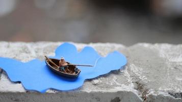 un' miniatura figura di un' pescatore pesca nel un' fiume visualizzato su blu carta ritagli. foto