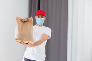 consegna uomo Tenere carta Borsa con cibo su bianca sfondo, cibo consegna uomo nel protettivo maschera foto