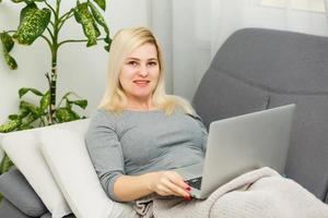 giovane donna Lavorando su un' il computer portatile a casa. ragazza seduta su un' letto con un' computer. quarantena, restare casa concetto. coronavirus covid-19 foto