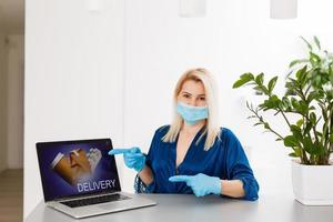 giovane donna a casa nel auto-quarantena ordine prodotti in linea consegna. in quarantena opera a partire dal casa. mascherato femminile nuovo vita con coronavirus isolamento. a distanza Lavorando su un' computer. pandemia stile di vita foto