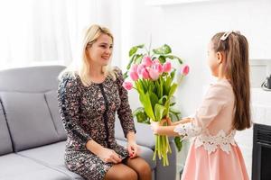 contento La madre di giorno. bambino figlia si congratula mamme e dà sua fiori tulipani foto