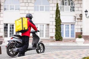 giallo consegna scatola su motociclo con consegna uomo nel davanti di Casa. foto