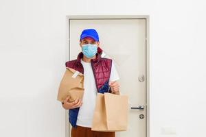 consegna uomo Tenere carta Borsa con cibo su bianca sfondo, cibo consegna uomo nel protettivo maschera foto