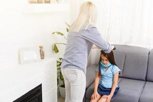 bellissimo madre intrecciare capelli di sua figlia nel il cucina. carino poco ragazza con lungo capelli. accogliente casa interno. contento e salutare famiglia. foto