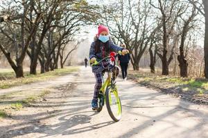 poco ragazza indossare medico maschera impedire influenza, inquinamenti e covid-19 equitazione bicicletta all'aperto. foto