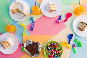 torta, caramella, cioccolato, fischi, stelle filanti, palloncini, succo su vacanza tavolo. concetto di figli di compleanno festa. Visualizza superiore. foto