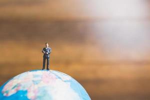 uomo d'affari in miniatura in piedi su una mappa del mondo globo con uno sfondo marrone foto