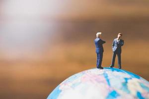 uomini d'affari in miniatura in piedi su una mappa del mondo globo con uno sfondo marrone foto