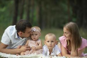 marito e moglie e loro poco bambini. famiglia ritratto nel natura. mamma e papà con loro fratello e sorella siamo dire bugie su il erba. giovane famiglia con bambini per un' camminare. foto